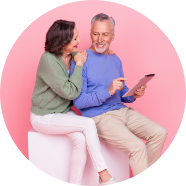 Retired Couple Sitting with Tablet Pink Background